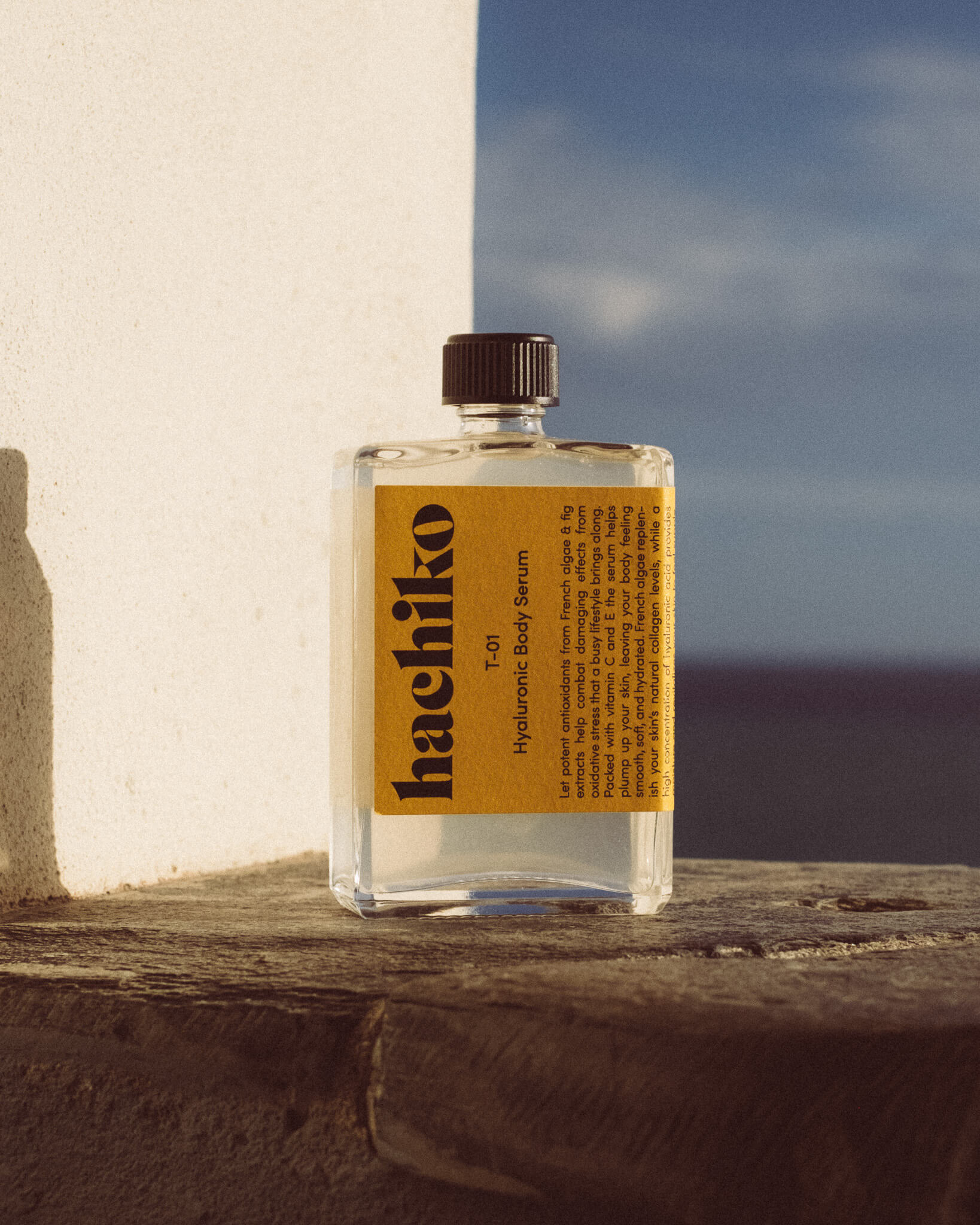T-01 Hyaluronic Body Serum von hachiko Berlin steht auf sonniger Terrasse mit Blick aufs Meer